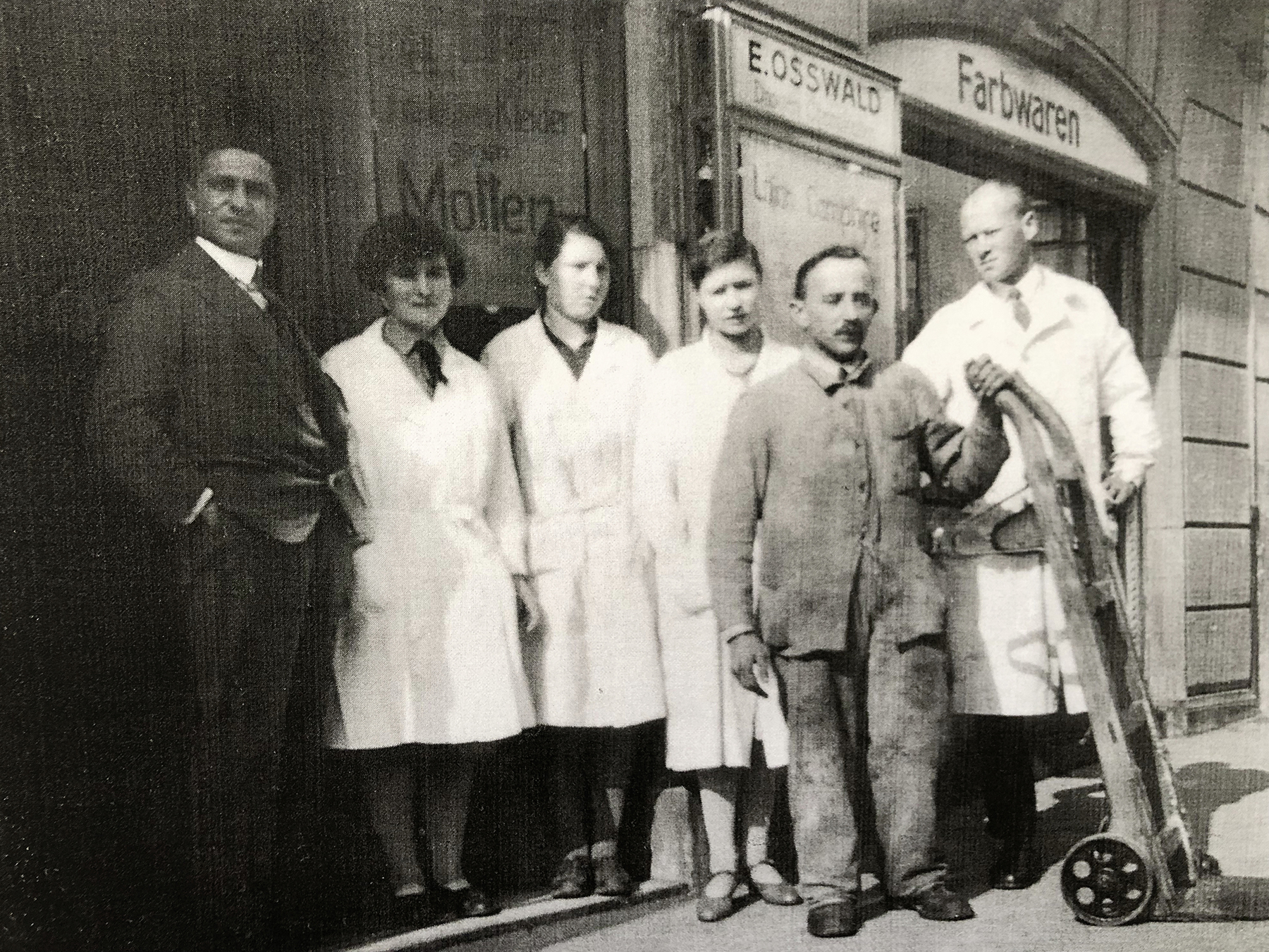 Boris Dreiding (links) und Ernst Osswald (rechts) mit Angestellten vor dem Kolonialwarengeschäft, Datum unbekannt. (Bild: Osswald, Zürich) 
